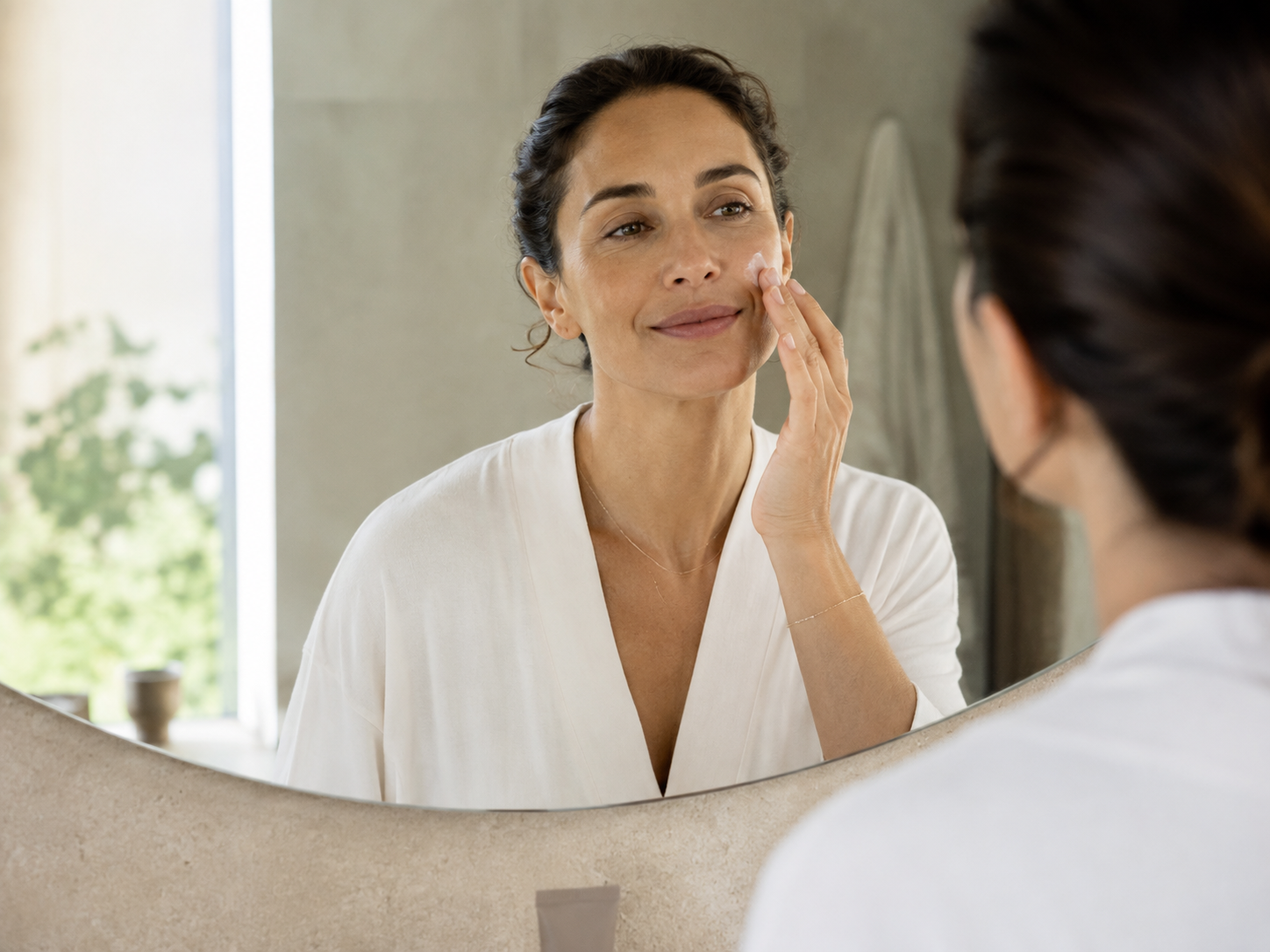Femme appliquant un soin hydratant sur son visage devant un miroir Image