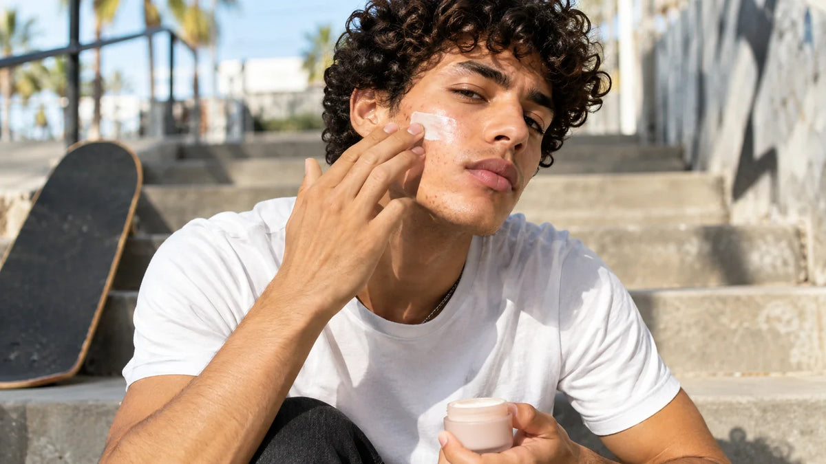 Jeune homme appliquant un soin visage en extérieur avec quelques imperfections visibles