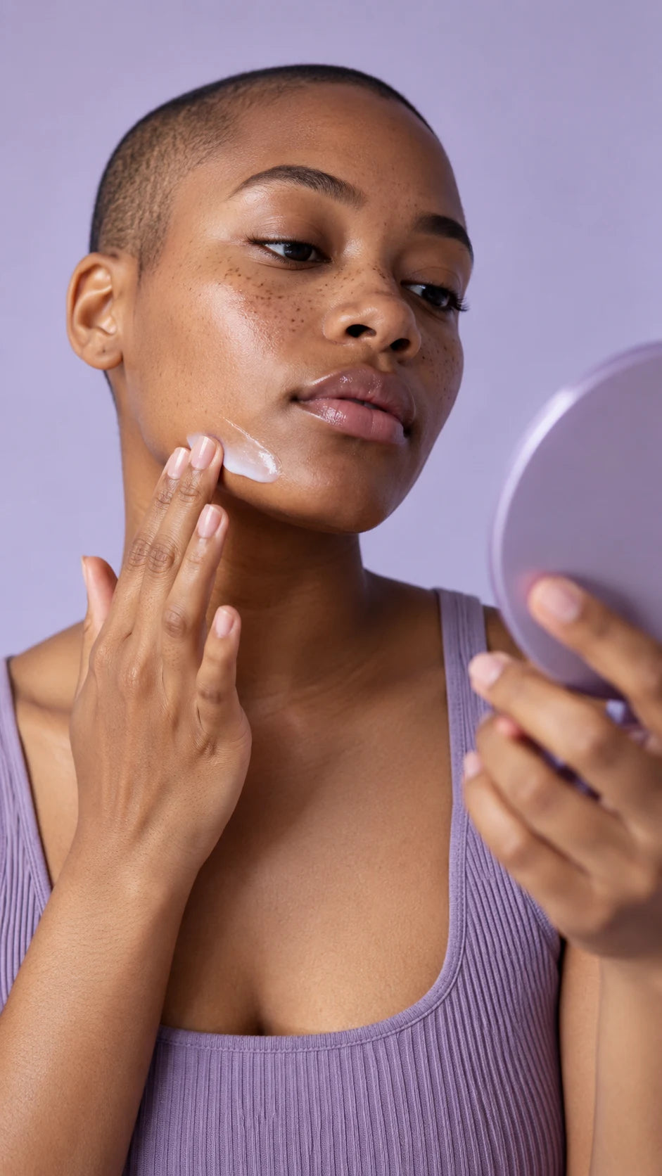 Jeune femme appliquant un soin visage devant un miroir sur fond lilas